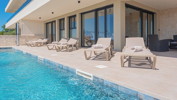 A poolside area with lounge chairs and a stone wall. - Aliara Panorama 1 
Luxusvilla (Vodice)