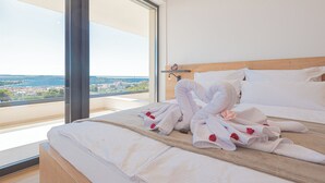 A hotel room with a large bed, a wooden headboard, and a view of a cityscape through a large window. - Aliara Panorama 1 
Luxusvilla (Vodice)