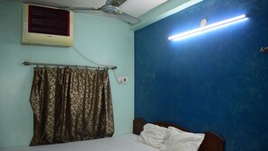 A bedroom with a bed, a ceiling fan, an air conditioner, and a wall-mounted light fixture. - New Balagi Guest House (Barakpur)