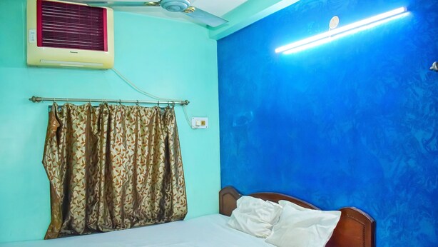 A room with a bed, a ceiling fan, an air conditioner, and patterned curtains. - New Balagi Guest House (Barakpur)