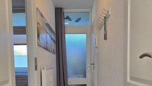 En smal gang med en bænk, en radiator, en dør med matteret glas og en telefon på væggen.