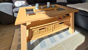 En moderne stue med et træbord, en sofa og et stort vindue med persienner.