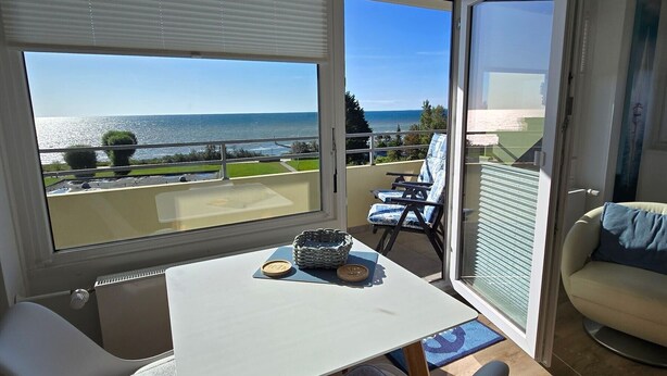 A modern room with a table and chairs, a view of the sea, and a balcony with outdoor furniture.