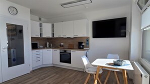 A modern kitchen with white cabinets, a built-in oven, and a dining area with a table and chairs.