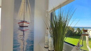 A room with a large window, a sailboat painting, and a view of the sea.