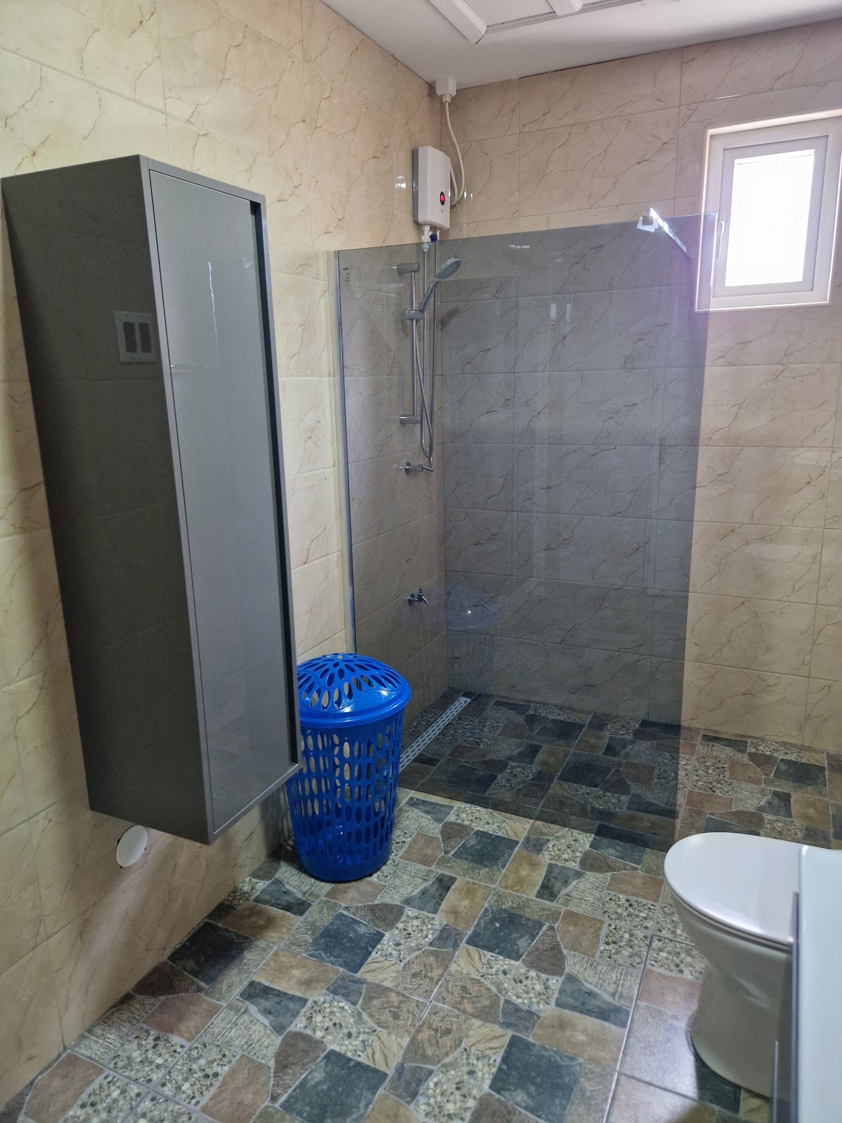 Casa de banho com chuveiro, sanita e cesto de roupa azul.