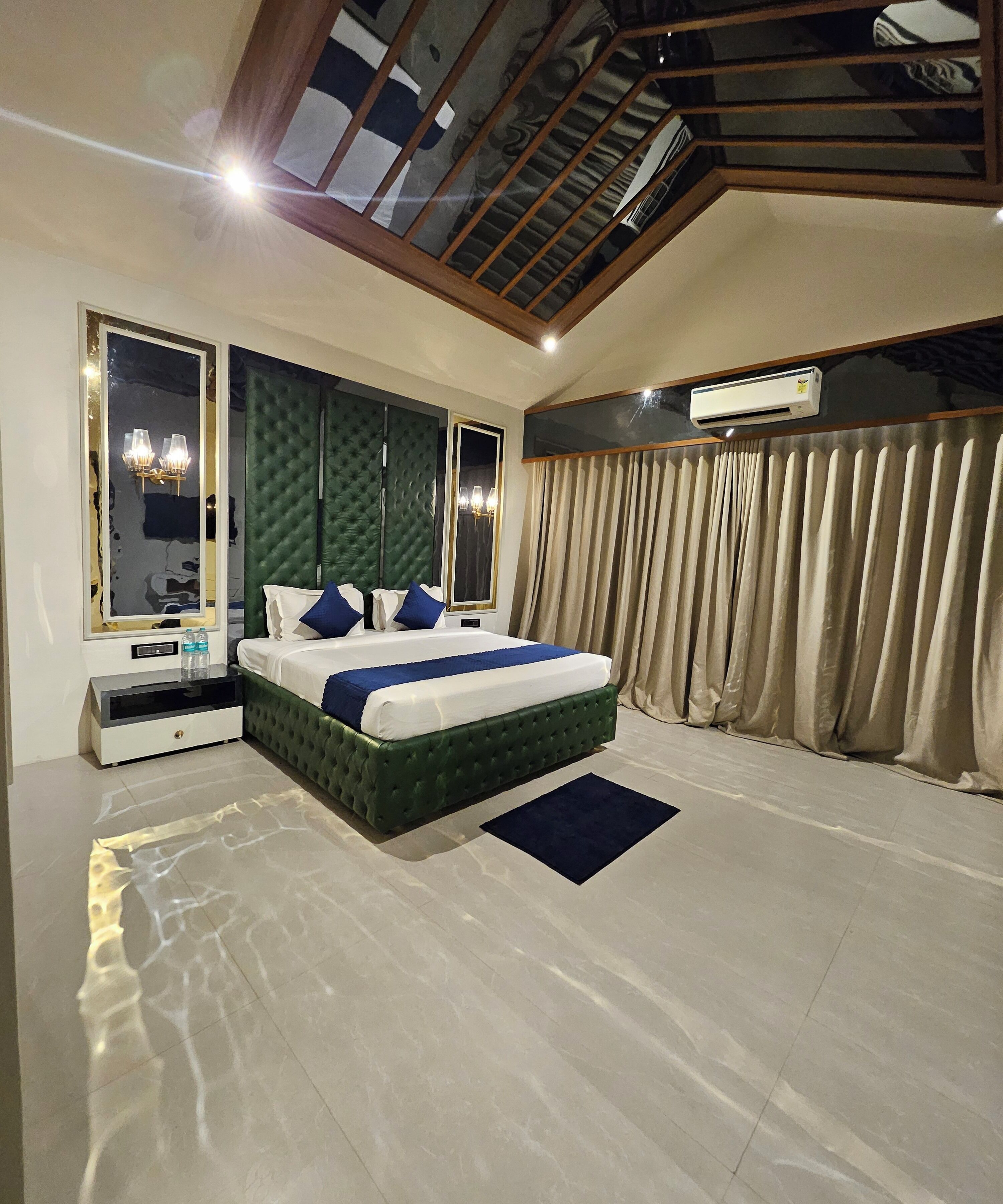 A modern bedroom with a large bed, a green tufted headboard, a large mirror, and a ceiling fan.