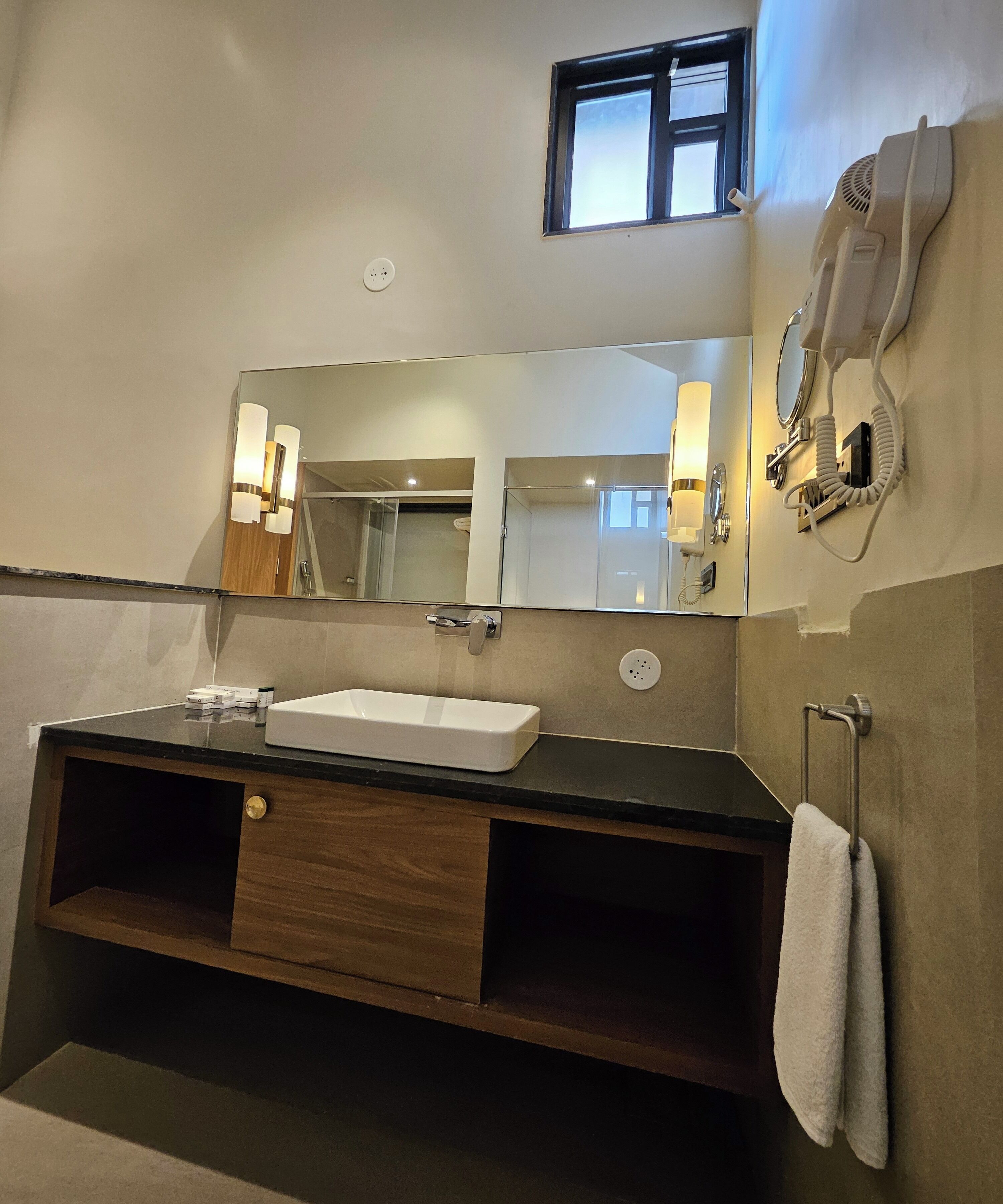 A modern bathroom with a large mirror, a sink, a towel rack, and a hairdryer.