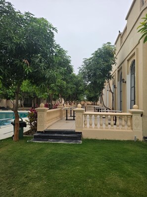 A courtyard with a swimming pool, a fountain, and a building with a balcony. - M Farm Resort (Rajkot)