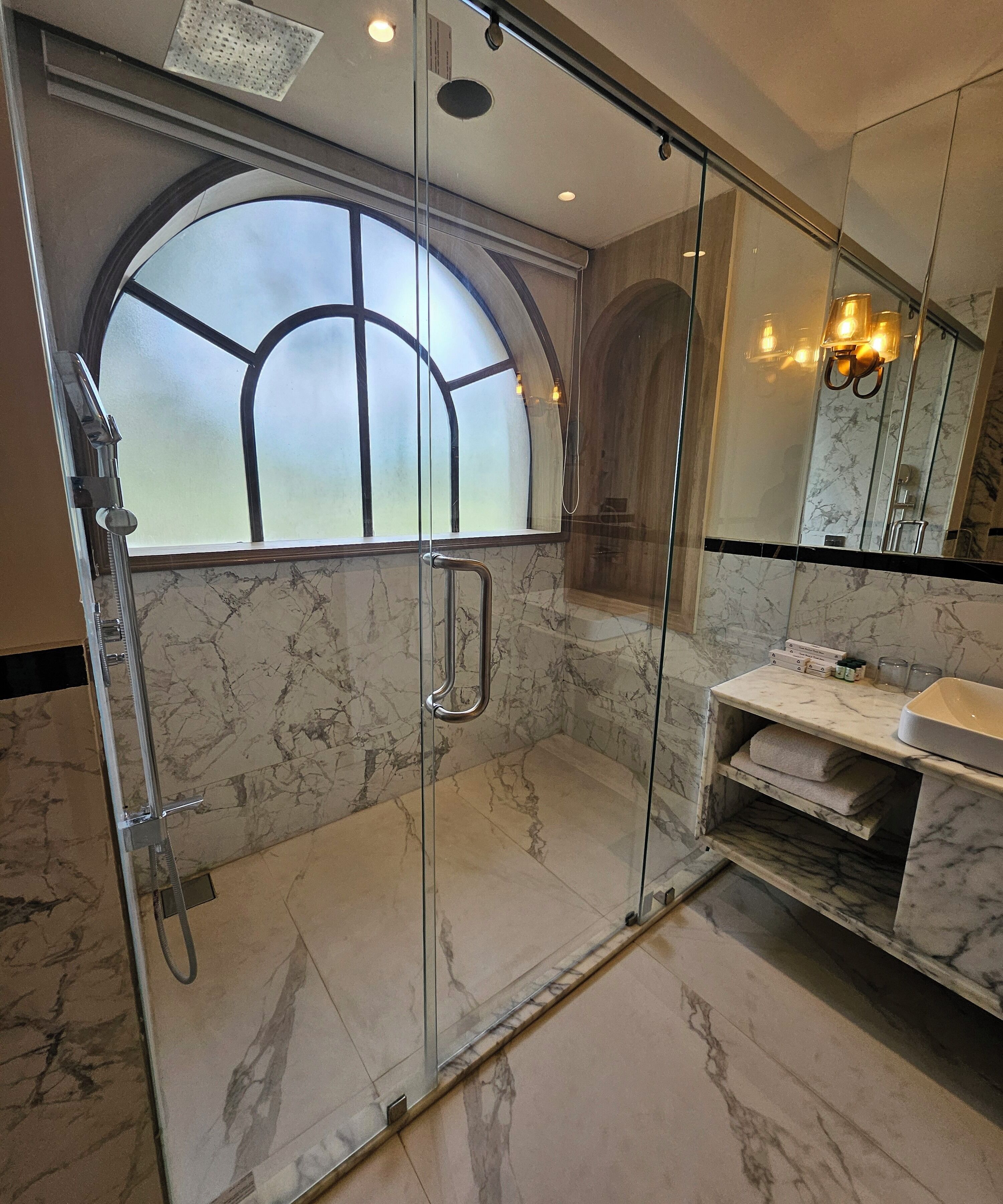 Ein modernes Badezimmer mit einer gläsernen Duschkabine, Marmorboden und einem großen Bogenfenster.