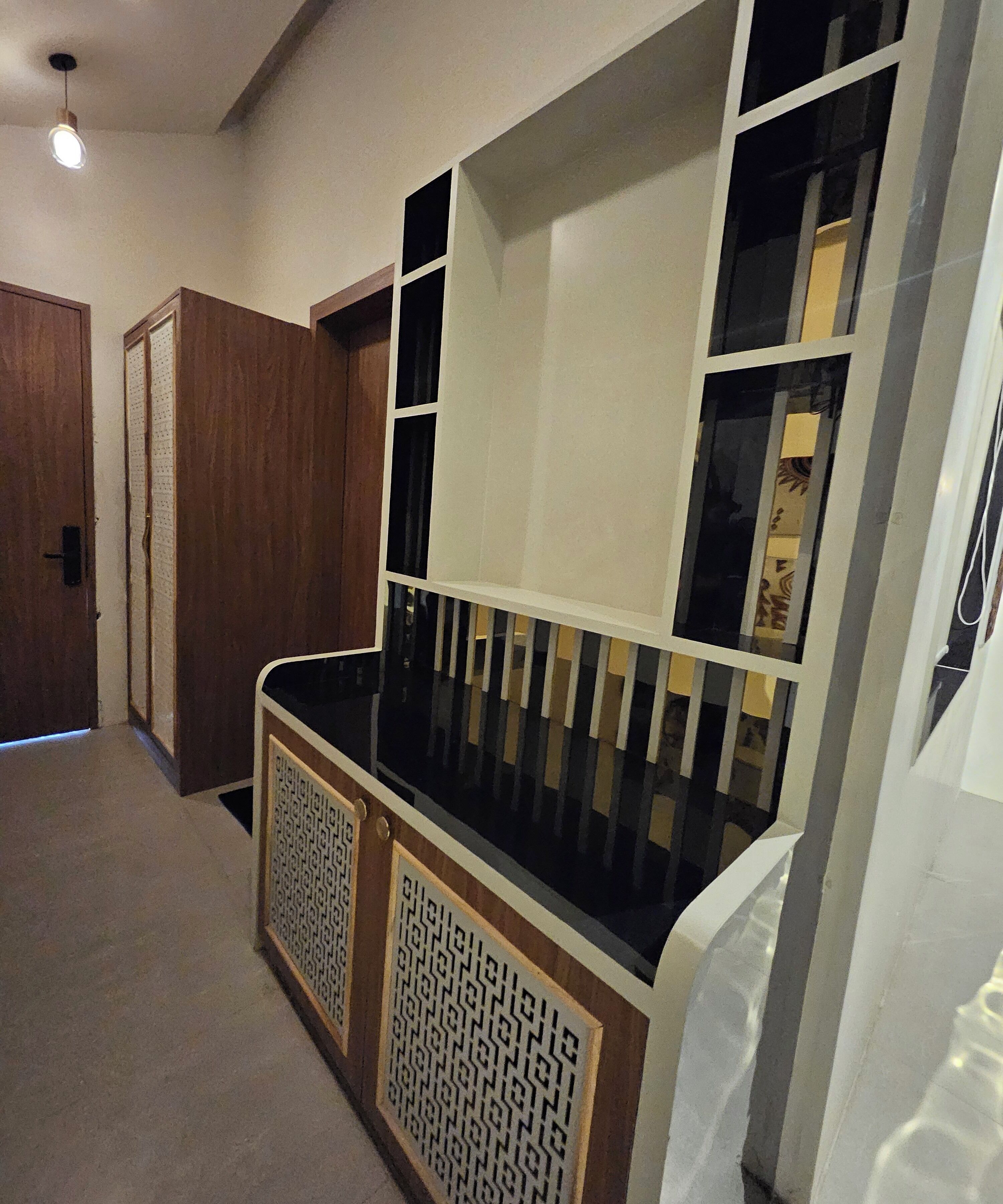 A hallway with a wooden door, a white wall, and a black and white patterned cabinet.