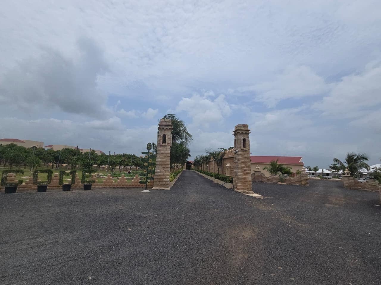 A paved entrance with stone pillars, a pathway leading to a building with a red roof, and a clear sky.