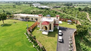 A large, historic building with a courtyard, a parking area, and a view of the surrounding countryside. - M Farm Resort (Rajkot)