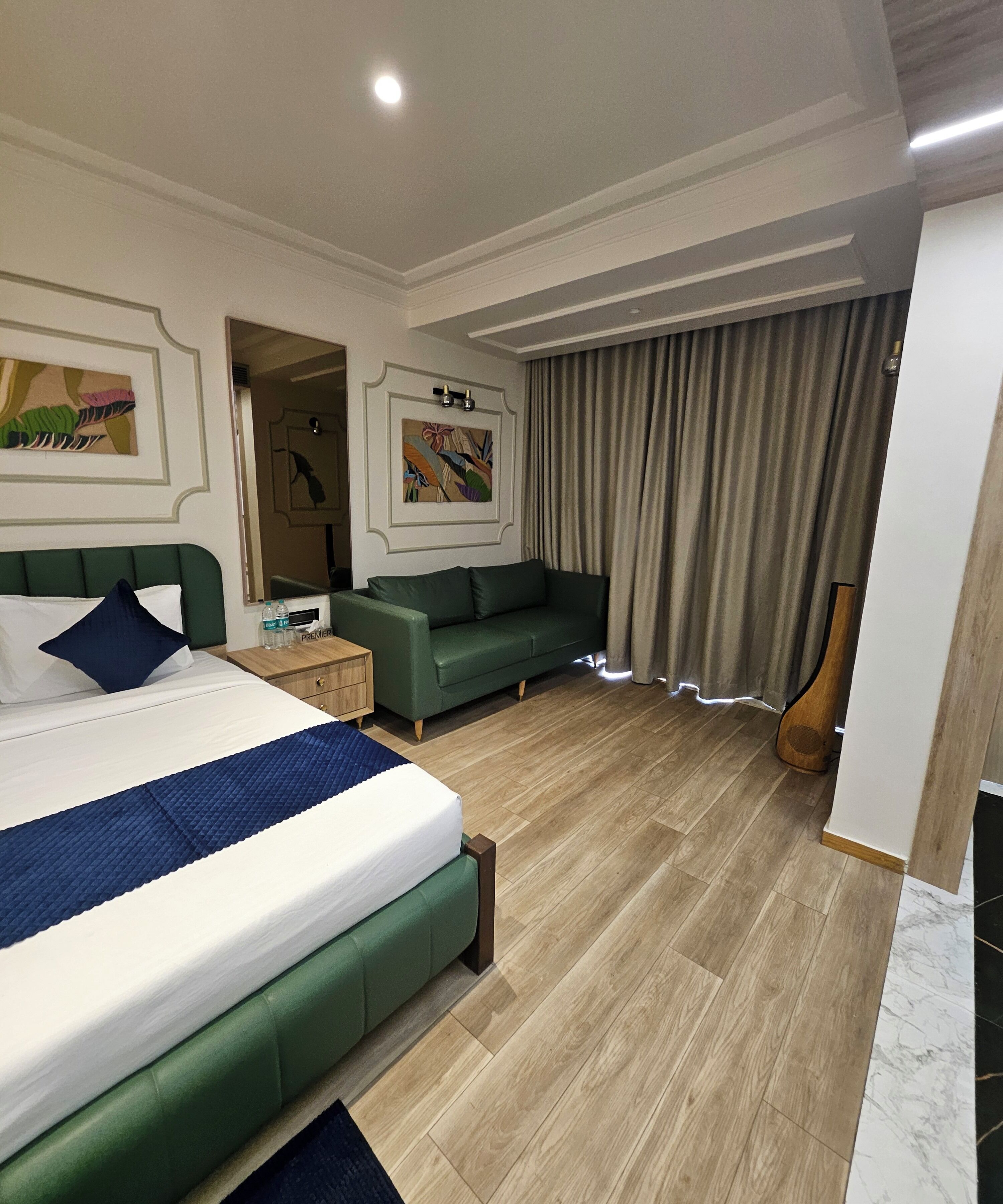 A hotel room with a large bed, a green sofa, a wooden guitar, and a painting on the wall.