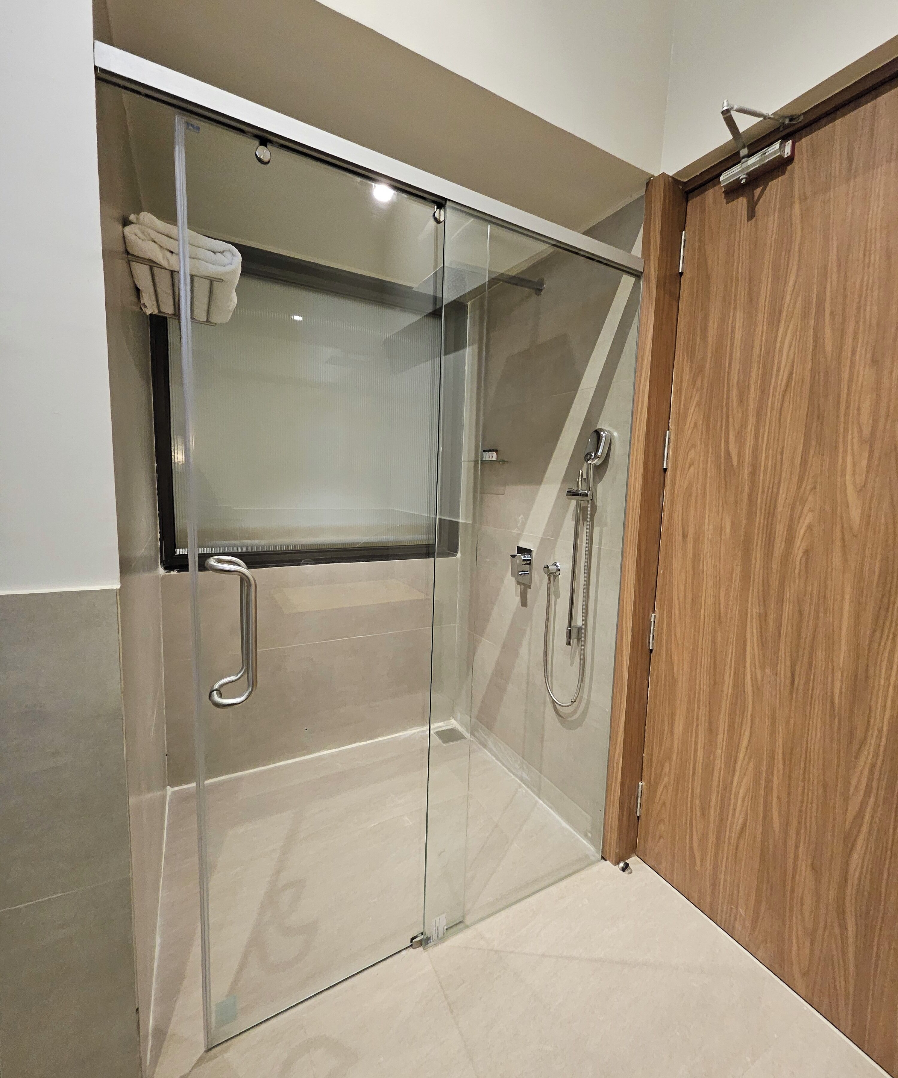 Un área de ducha con paredes de vidrio, una puerta de madera y un perchero para toallas.