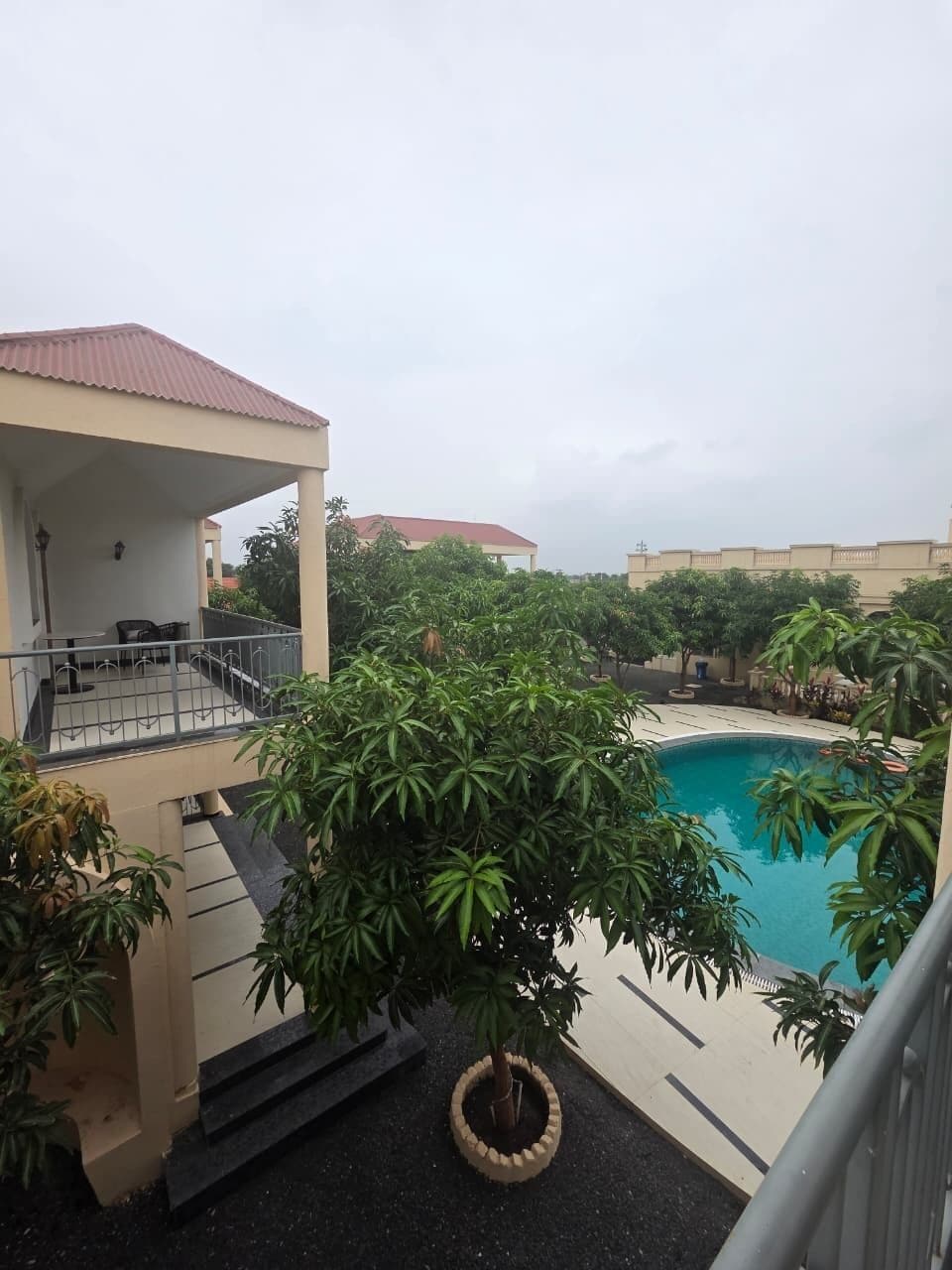 Zona residencial amb piscina envoltada de vegetació i un edifici amb balcó.