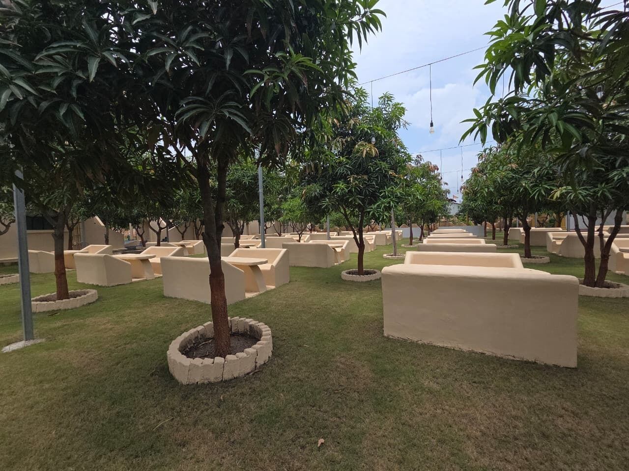 A landscaped area with trees and planters, a clear sky, and a pathway leading through the space.