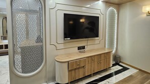 A modern living room with a large flat-screen TV mounted on the wall, a wooden cabinet below, and decorative panels on the walls. - M Farm Resort (Rajkot)