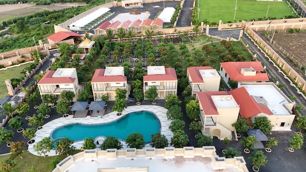 An aerial view of a resort with multiple buildings, a swimming pool, and a fortified wall. - M Farm Resort (Rajkot)