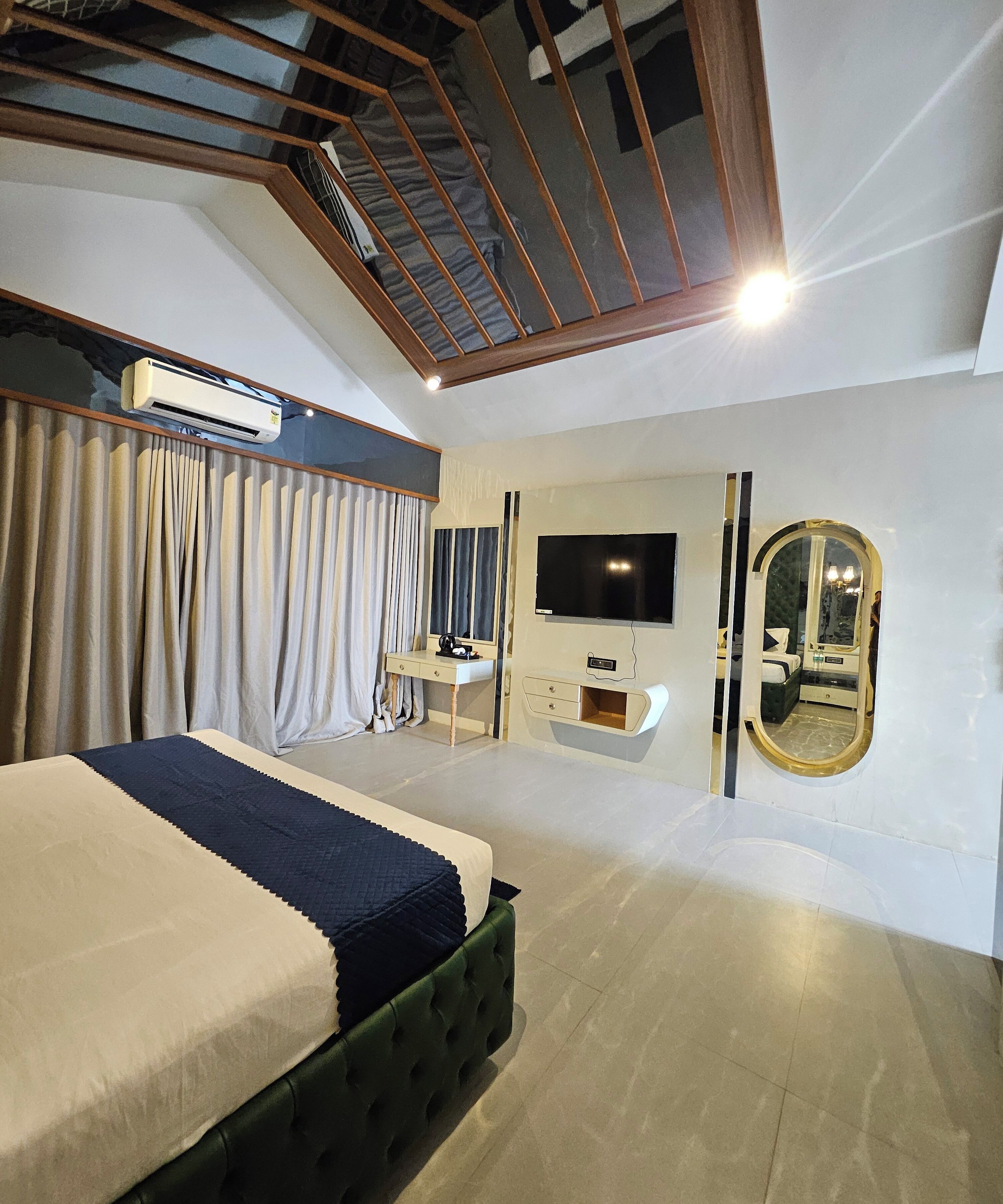 Un dormitorio moderno con cama, tocador, televisión y un espejo grande.