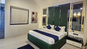 A bedroom with a large bed, a nightstand, a dresser, and a mirror. - M Farm Resort (Rajkot)