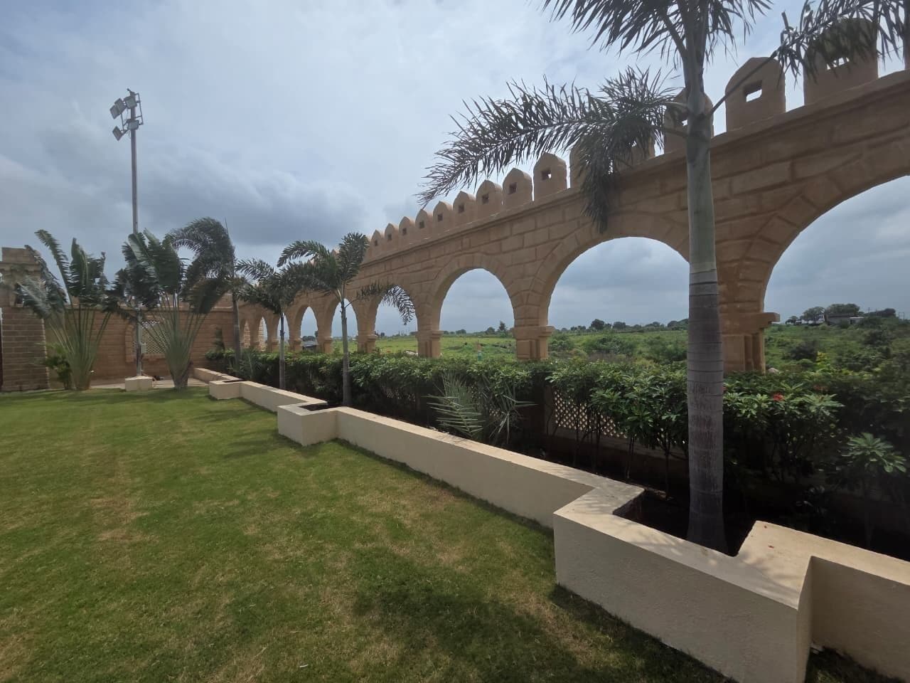 A pathway with arches, palm trees, and a grassy area.