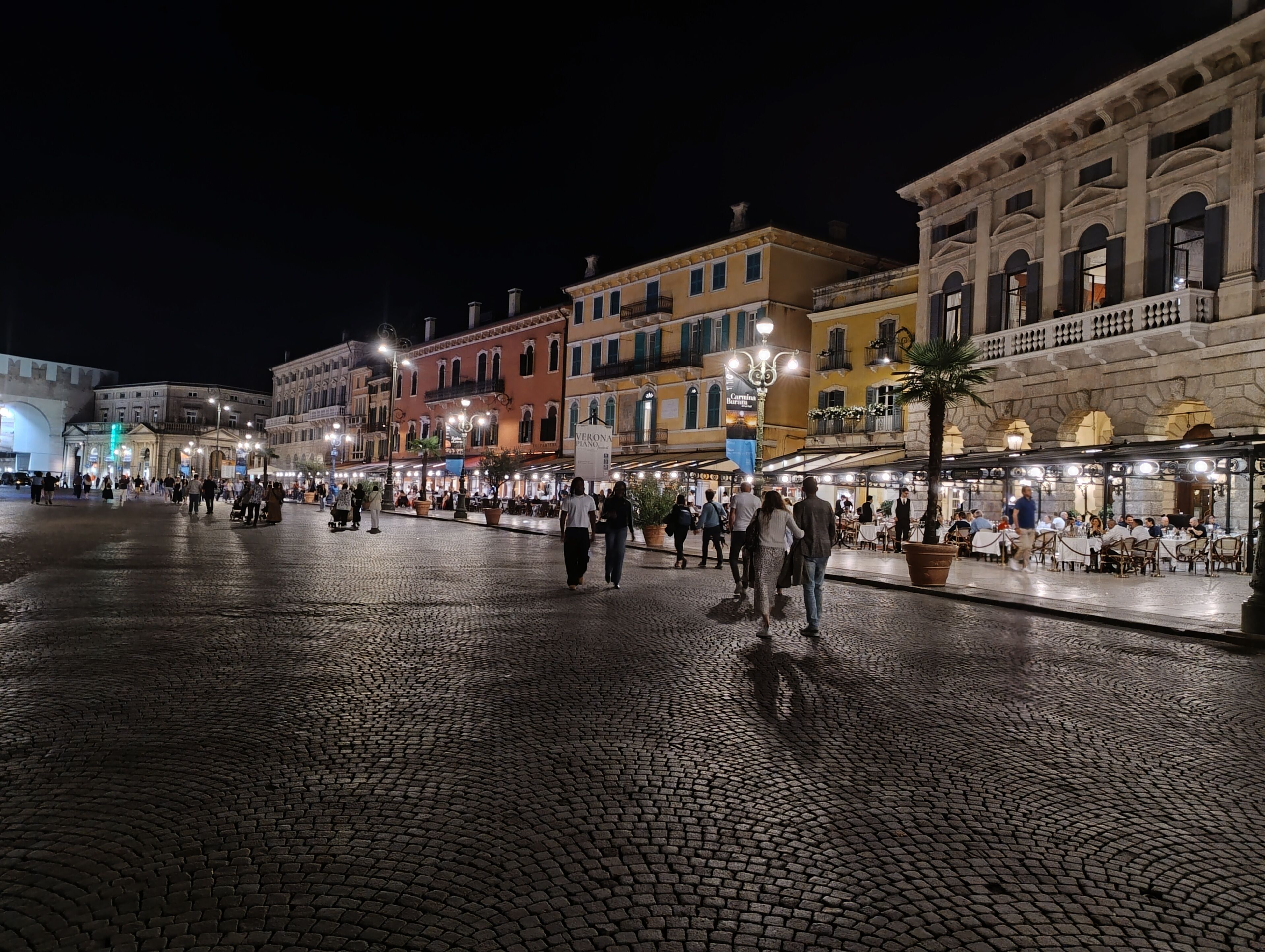 A cobblestone square with historic buildings, outdoor seating, and a fountain.