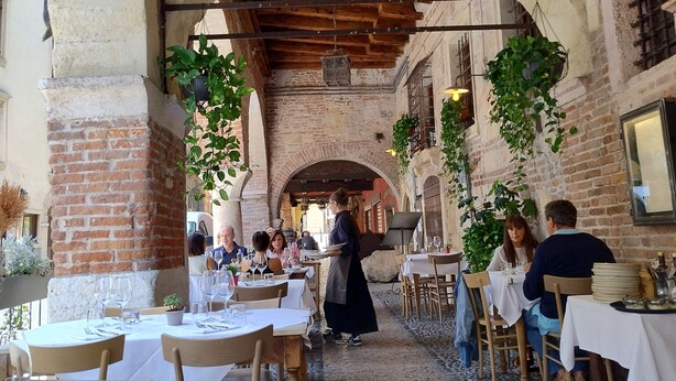 An outdoor dining area with brick arches, tables set with white tablecloths, and hanging plants. - One step away from Juliet's House, Piazza Erbe and Ponte Pietra quiet area (Verona)