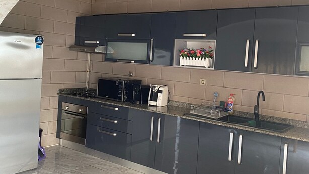 Une cuisine moderne avec des meubles de couleur sombre, un réfrigérateur en acier inoxydable, un four à micro-ondes et un four encastré.