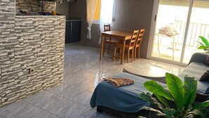 Un salon moderne avec un mur d’accent en pierre, un téléviseur à écran plat, un coin repas avec des meubles en bois et une grande plante en pot.