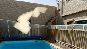Une piscine rectangulaire à l’eau d’un bleu limpide, entourée d’une clôture en bois et d’une terrasse en pierre.