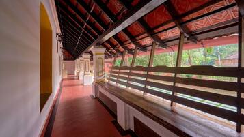 A corridor with a red-tiled floor, white pillars, and a wooden bench.