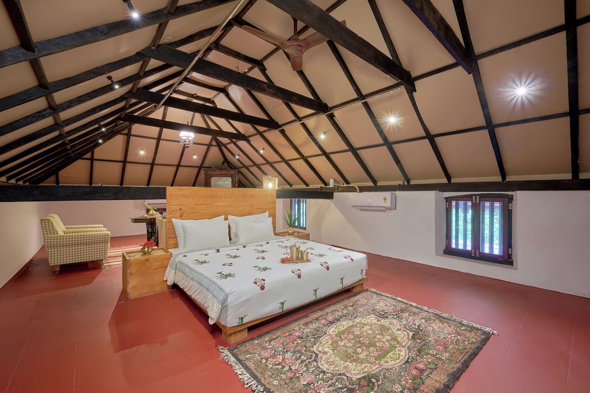 Ein Schlafzimmer mit geneigter Decke, einem Bett mit floralem Bettbezug, einem hölzernen Nachttisch, einem Sessel und einem gemusterten Teppich.
