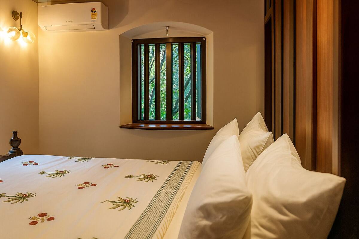 Ein Schlafzimmer mit einem Bett, einem Fenster mit vertikalen Jalousien, einer Wand-Klimaanlage und einer Wandleuchte.