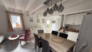 A dining area with a wooden table, chairs, and hanging pendant lights. - Welcome to the Terns! The dune house. (Barneville-Carteret)