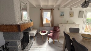 A cozy kitchen with a stone fireplace, a dining area with a wooden table and chairs, and a window with curtains. - Welcome to the Terns! The dune house. (Barneville-Carteret)