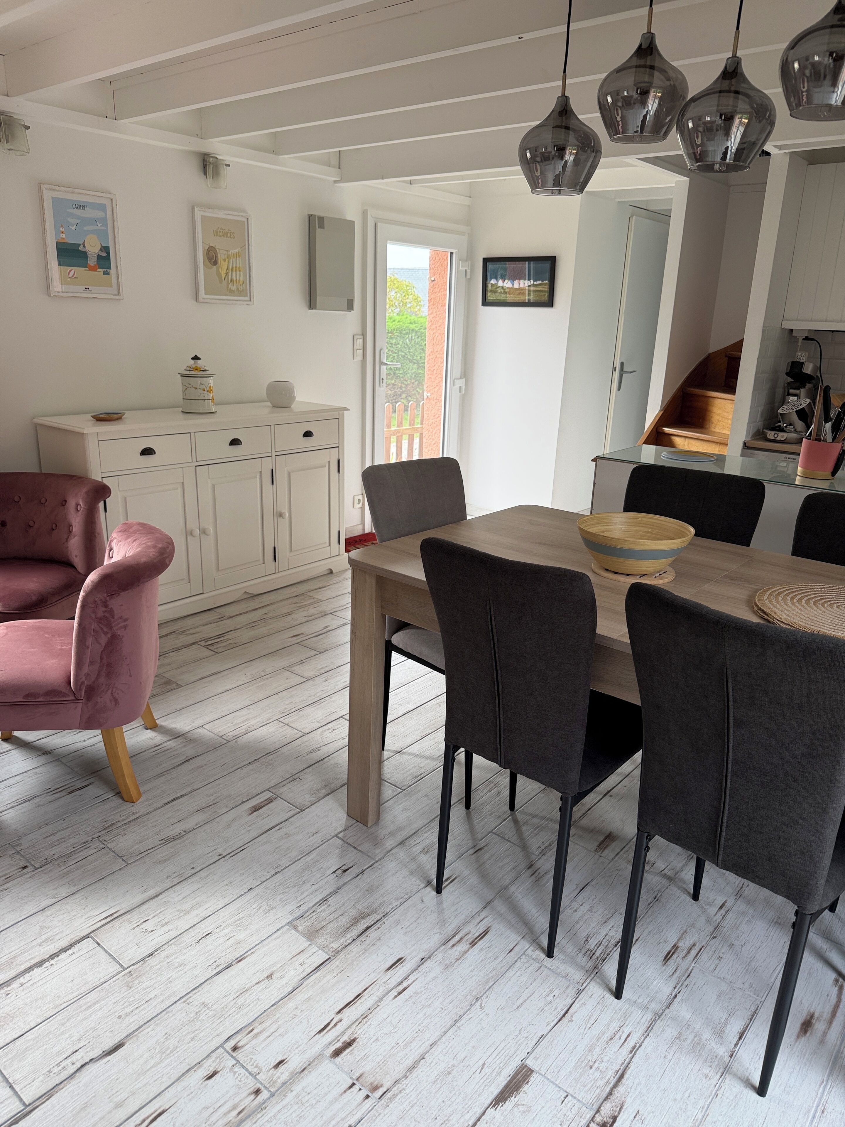 A dining area with a wooden table and chairs, a pink armchair, and a white cabinet with a coffee machine.
