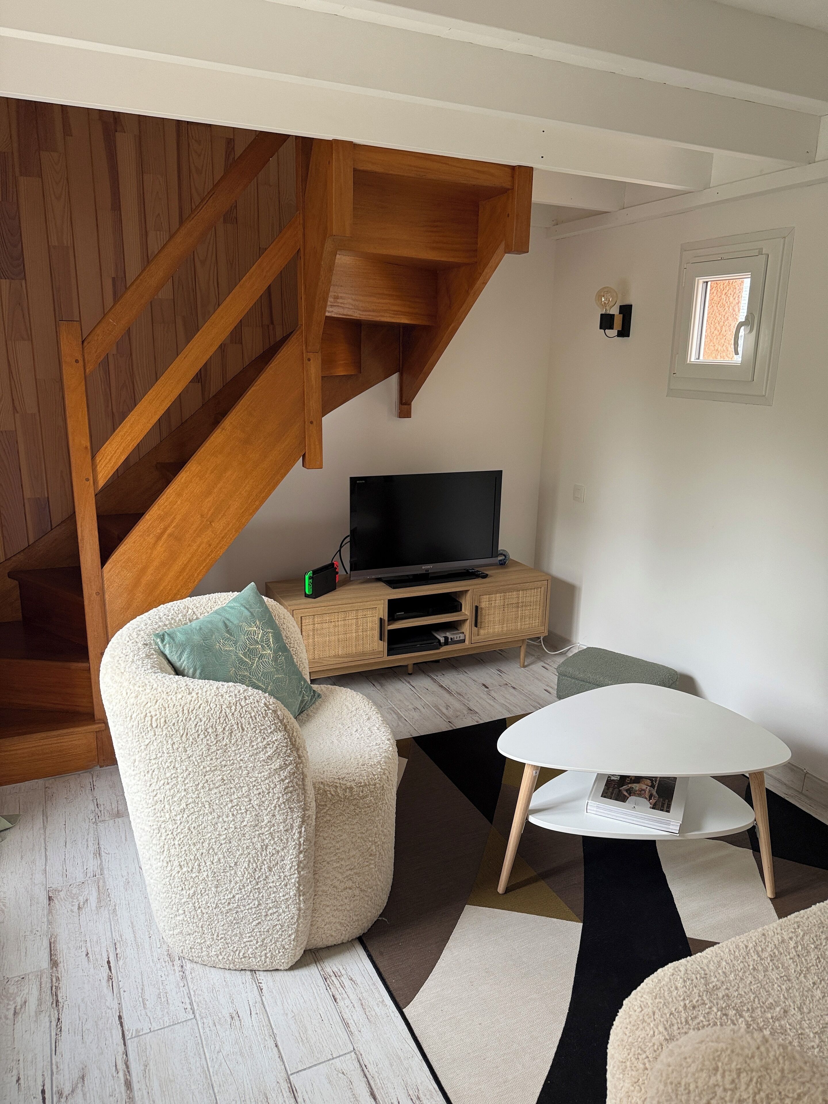 A living room with a wooden staircase, a flat-screen TV on a wooden cabinet, and a white coffee table.