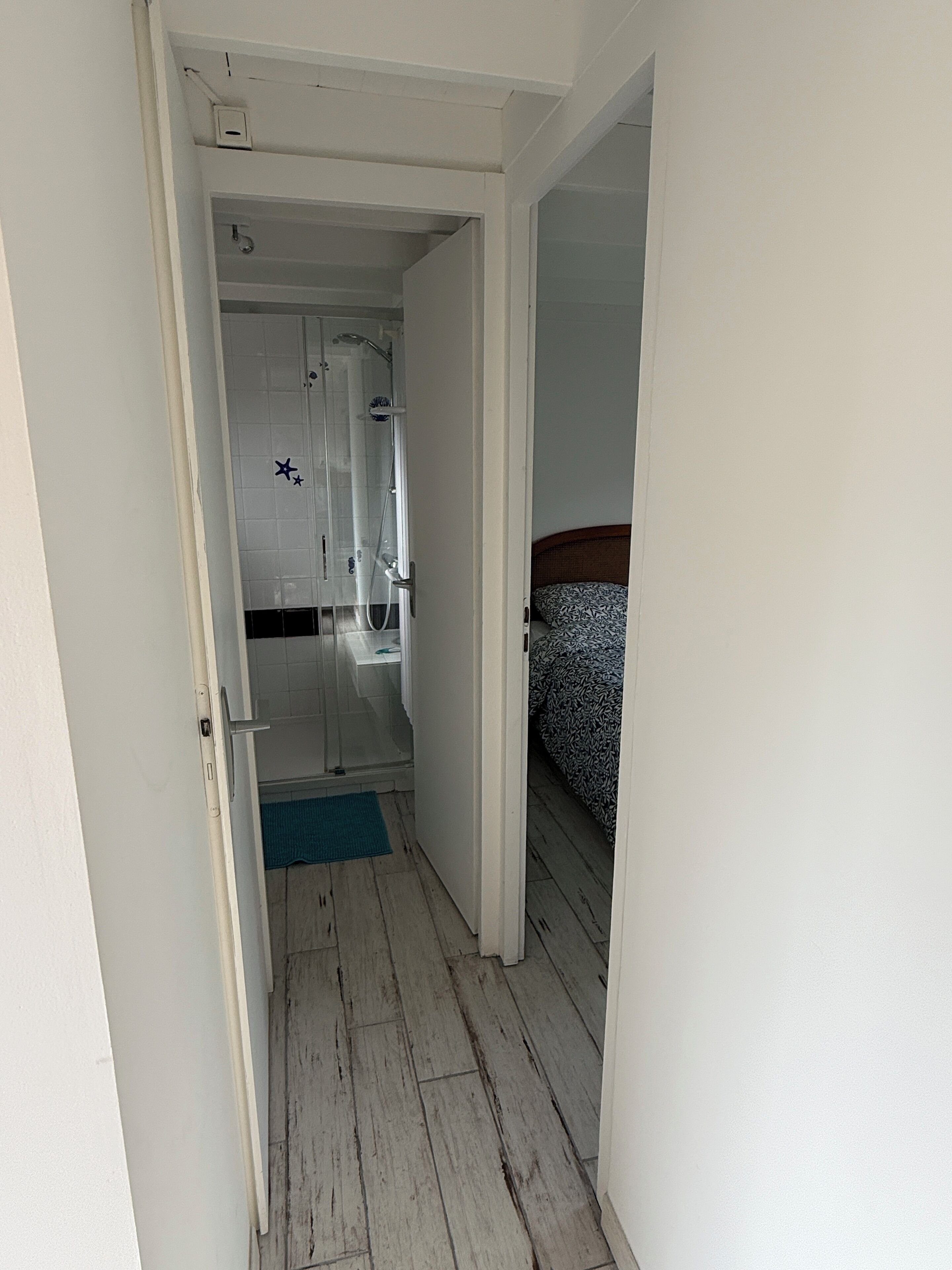 A narrow hallway leading to a bathroom with a shower and a bed with patterned bedding.