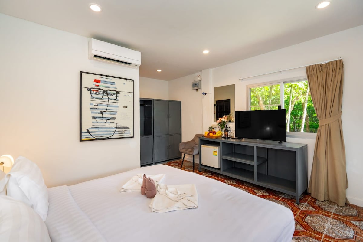 A hotel room with a bed, a desk with a television, a wardrobe, and a window with curtains.