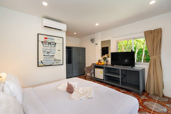 Quarto de hotel com cama, escrivaninha com televisão, guarda-roupa e janela com cortinas.