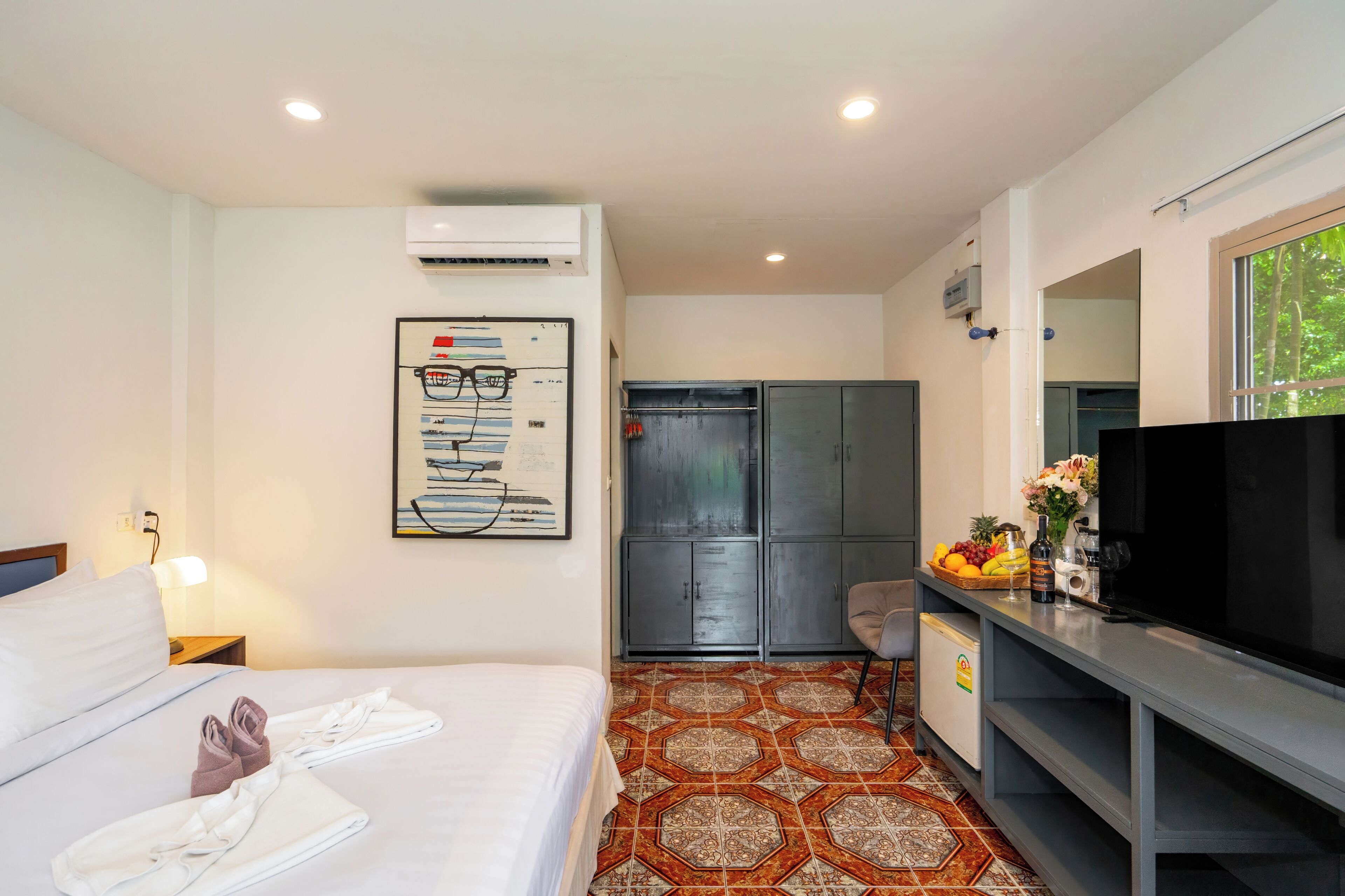 A hotel room with a bed, a desk with a television, a wardrobe, and a bathroom visible through an open door.