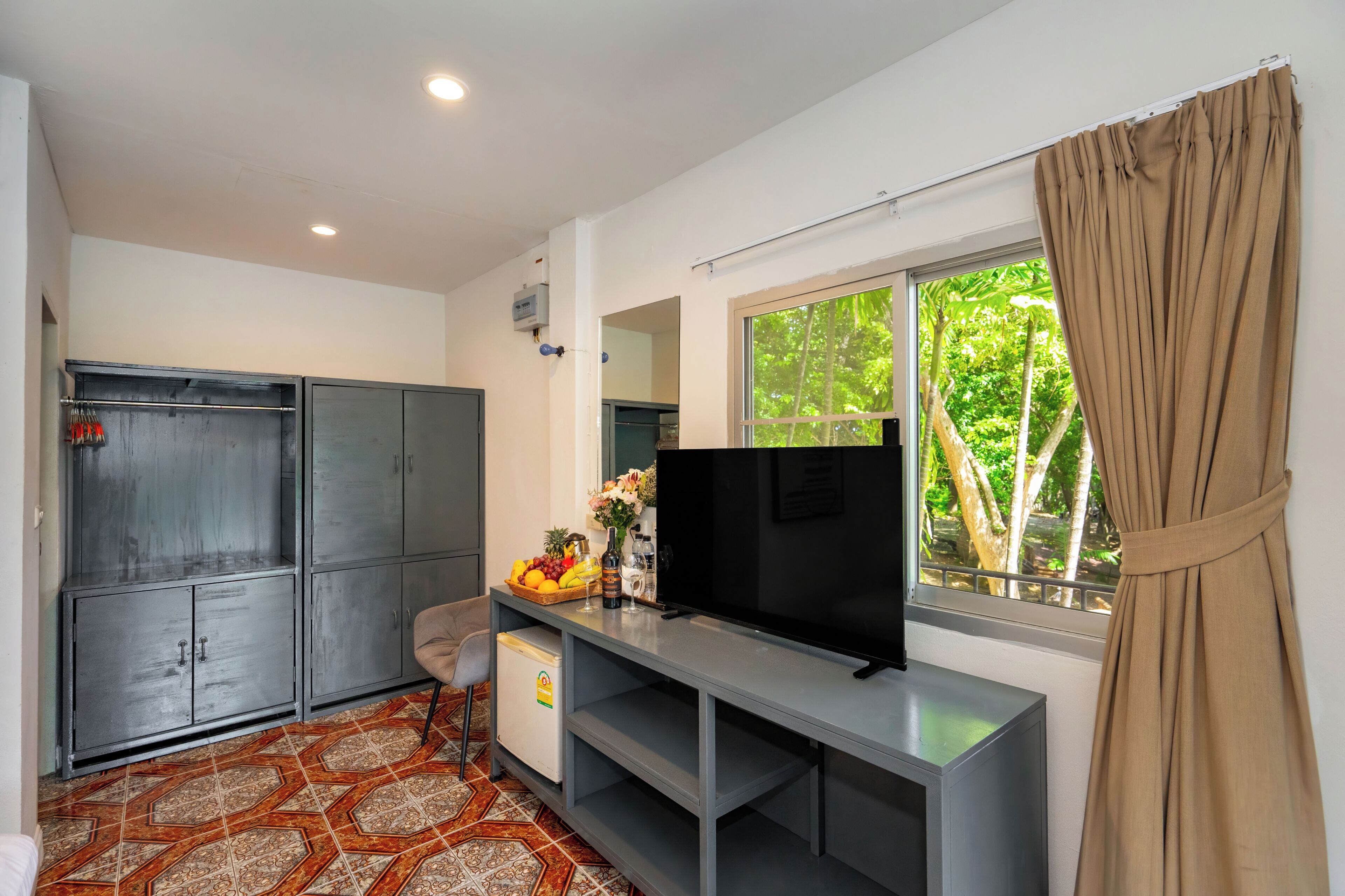 Una habitación con televisión, refrigerador pequeño, armario, ventana con cortinas y piso estampado.