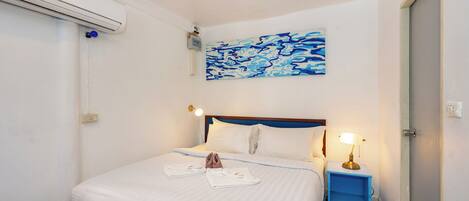 A hotel room with a bed, a painting, a bedside lamp, and a blue bedside table.
