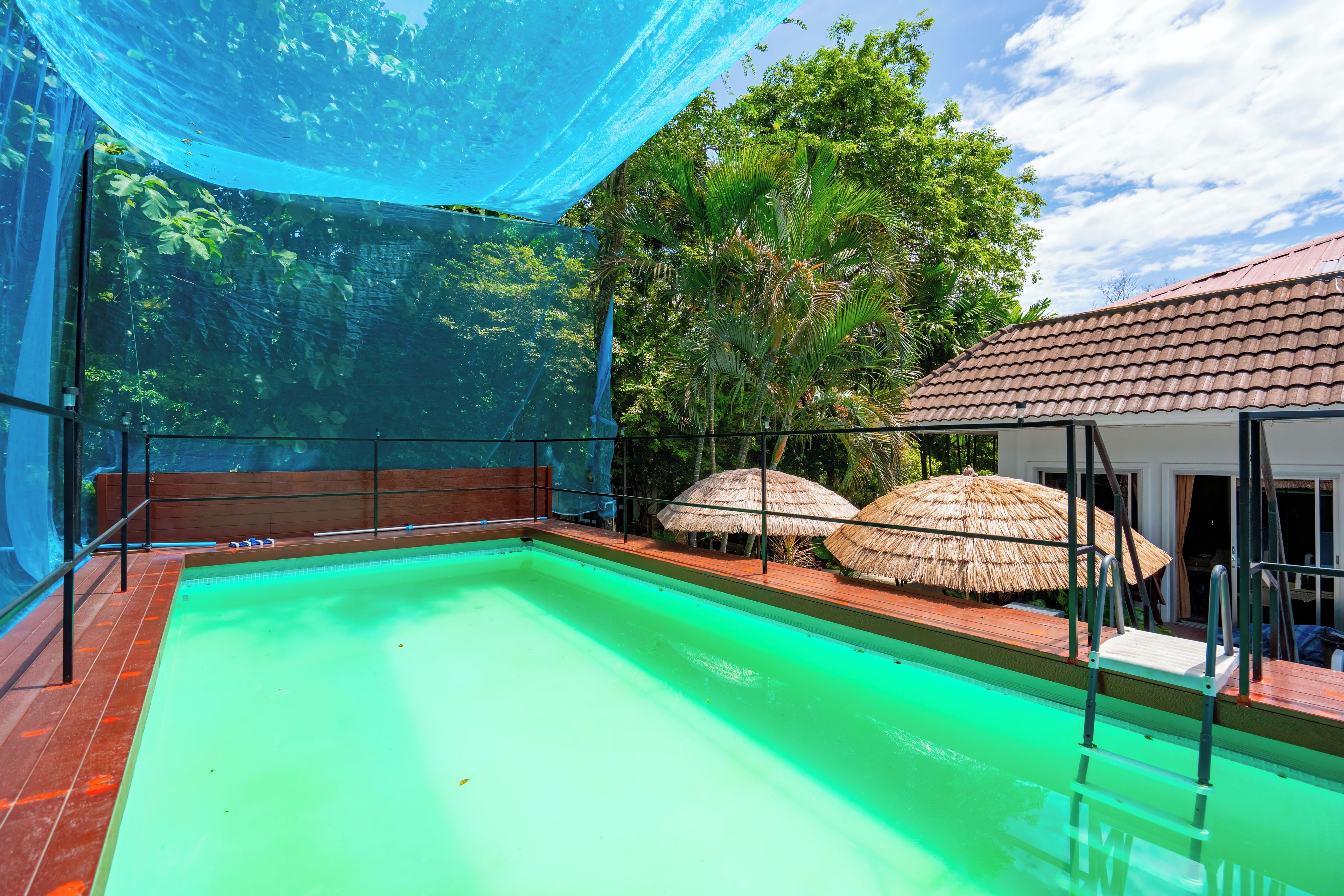A swimming pool with a wooden deck and a covered area with thatched umbrellas.