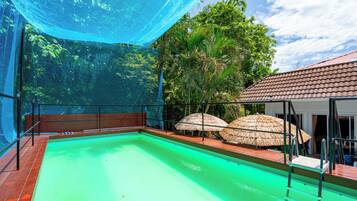 A swimming pool with a wooden deck and a covered area with thatched umbrellas.