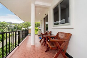 A balcony with a wooden table and chairs, a white railing, and a view of greenery and buildings. - Oceanview Bungalows by EAT, Karon Beach (Karon)