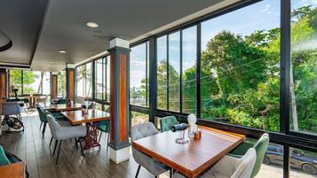 Un restaurante con amplios ventanales, mesas de madera y sillas verdes.