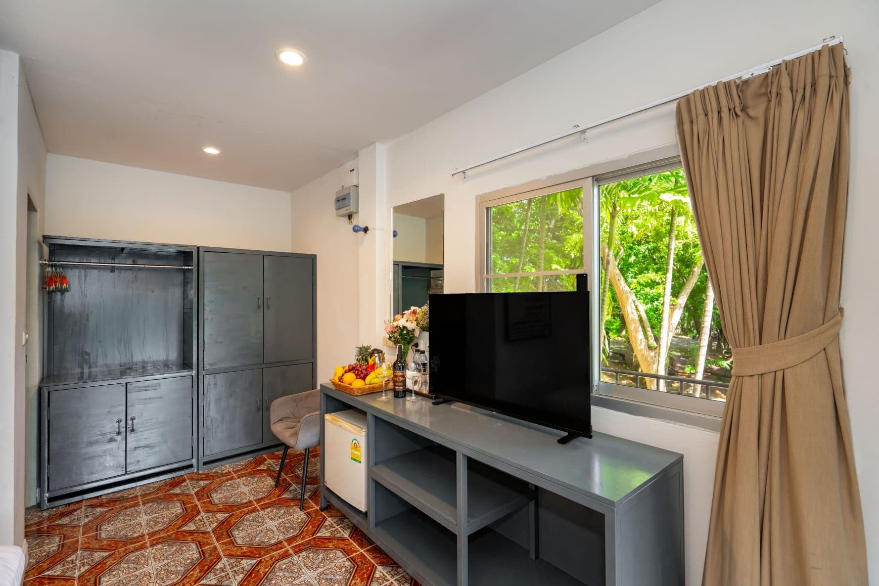 Una habitación con televisión, armario, escritorio con computadora y ventana con cortinas.