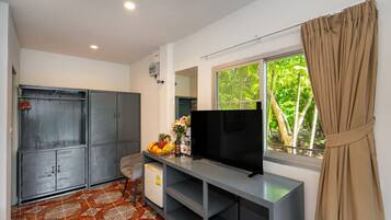 Una habitación con televisión, armario, escritorio con computadora y ventana con cortinas.